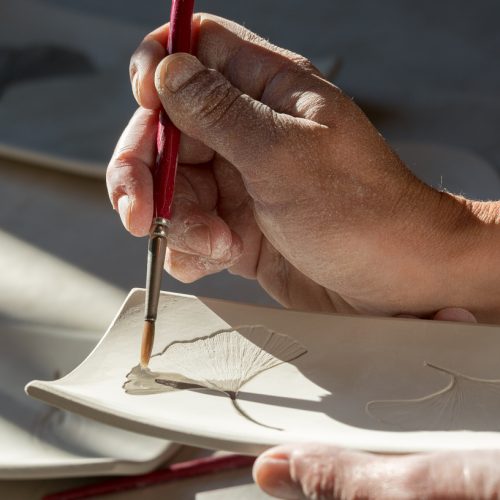 Anna paints glaze onto a dish. One of her hallmarks is to use leaves and flowers as stencils in the clay